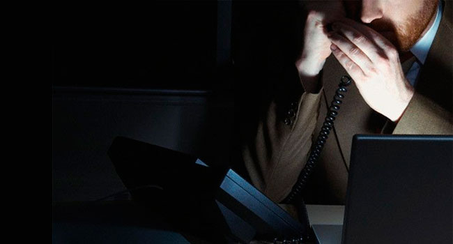 Imagem de uma pessoa de terno e gravata, ao telefone, num ambiente meio escuro, alusão a uma fraude ocupacional.